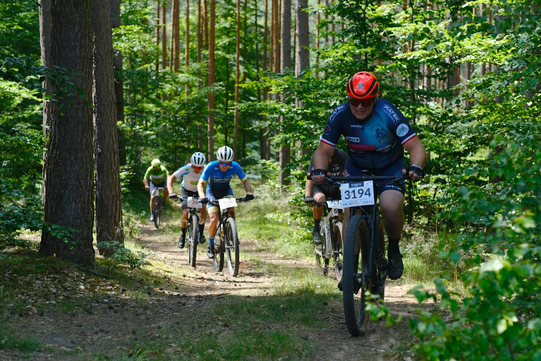Ilustracja przedstawiająca boisko Orlik z grupą osób ćwiczących, symbolizująca program "Sportowe weekendy na Orlikach" w Łomży.